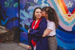 An LGBTQ+ couple embraces in front of a colorful wall
