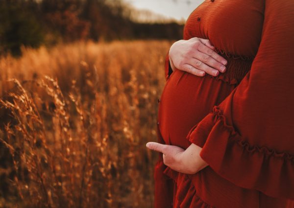 Birth parent in orange dress cradling pregnant belly.